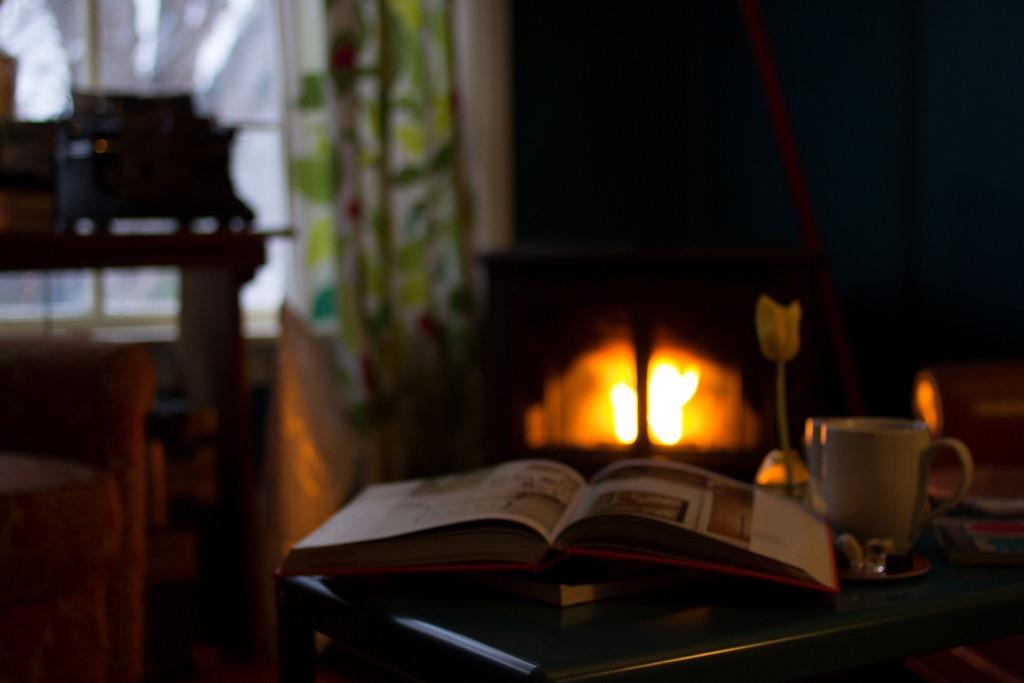 An open book on a coffee table in front of a wood burning fireplace.