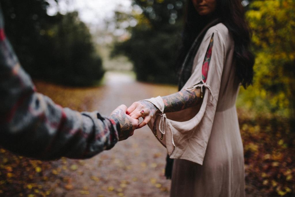A tattooed couple holding hands while on a walk.