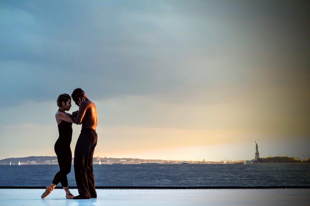 A couple doing ballet together with the statue of liberty in the background.