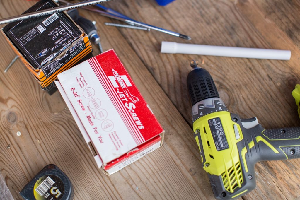 A table with a drill, nails, a measuring tape, and a screwdriver on it.