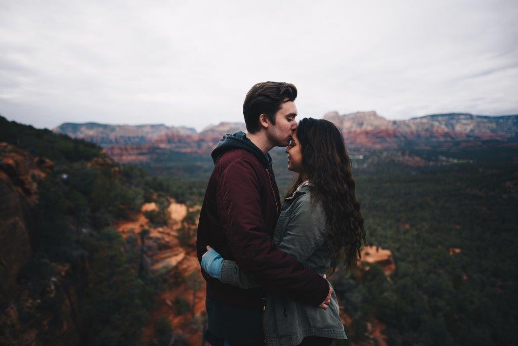 A man kissing a woman's forehead while on a hike.