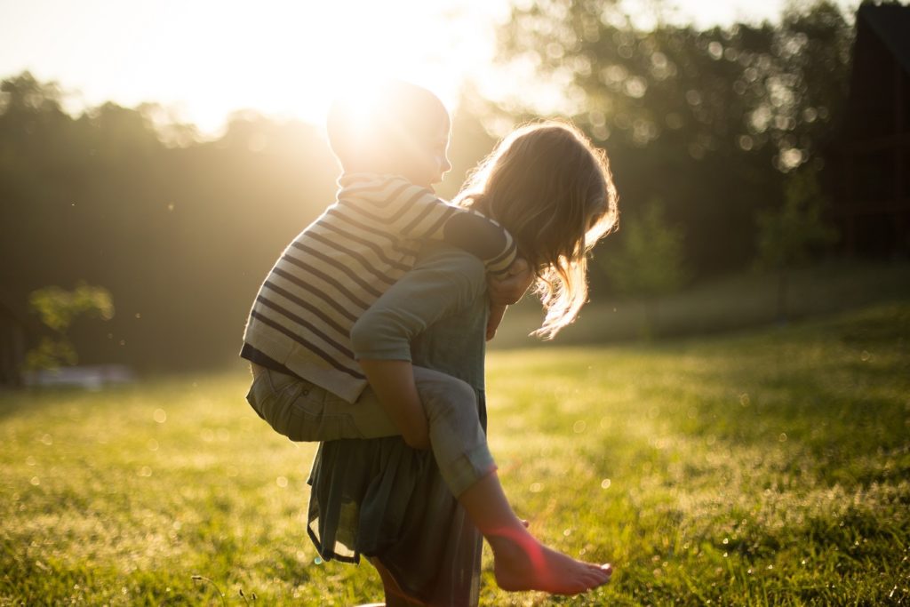 A little boy on a young girl's back in the yard.