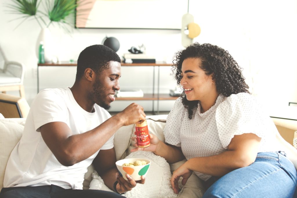 A couple snacking together on the couch.