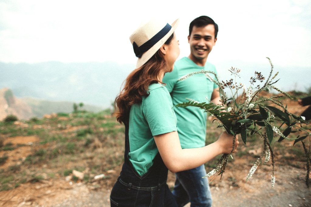 A couple smiling at each other and holding a bouquet of flowers.