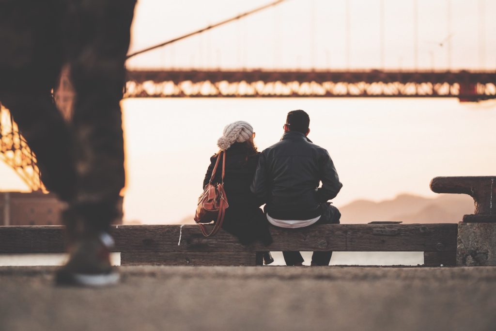 A couple sitting together looking at a bridge.