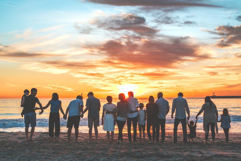 A large family standing on a beach holding hands at sunset.