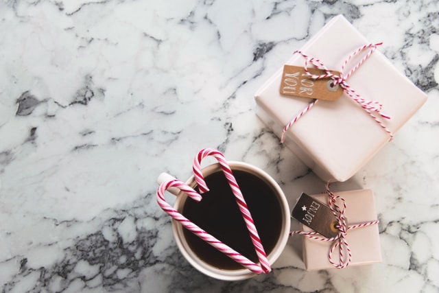 Candy canes on a mug with two wrapped Christmas gifts.
