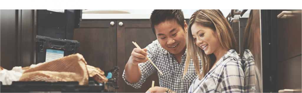 a young asian couple sitting on the floor of their kitchen eating Chinese food, cropped to show only faces