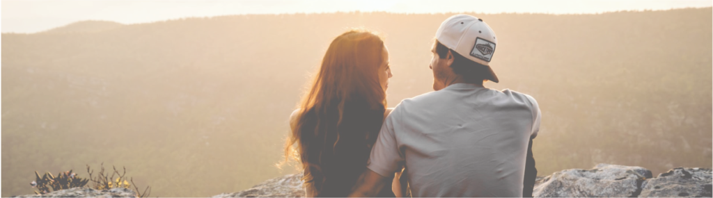 a couple sitting on a mountain top overlooking a mountain range, cropped to show only chest up