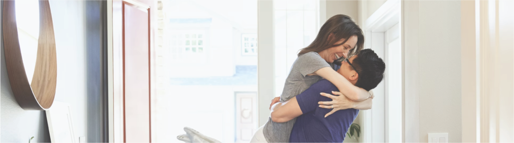 Smiling woman jumping into man's arms in brightly lit doorway