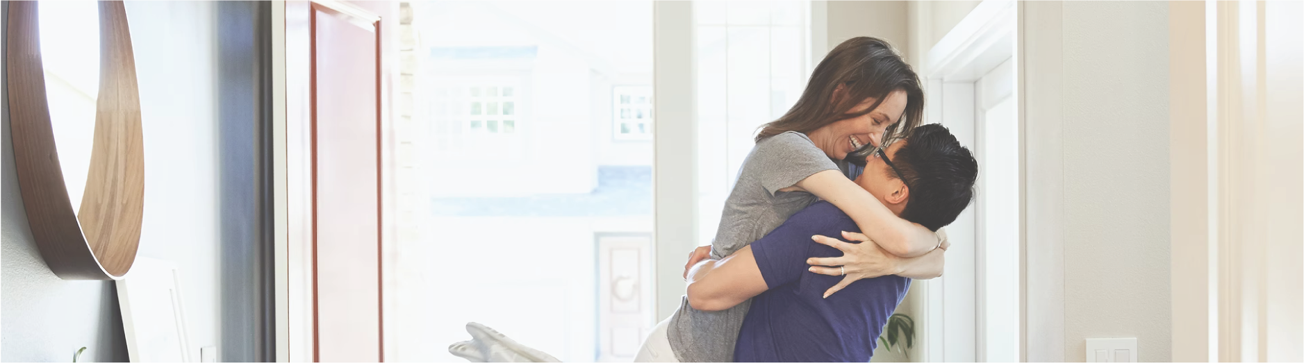 Smiling woman jumping into man's arms in brightly lit doorway