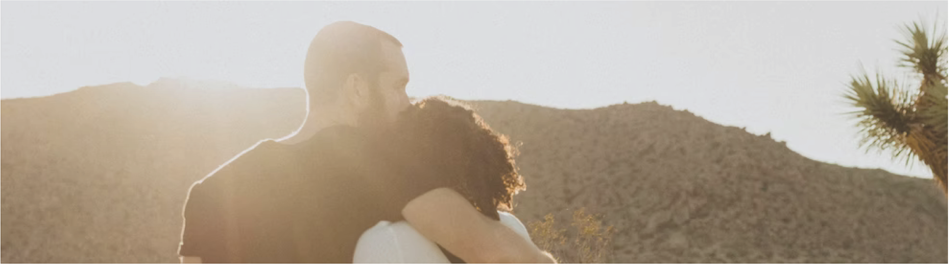 Couple walking into sunset, arms around shoulders, kiss on forehead