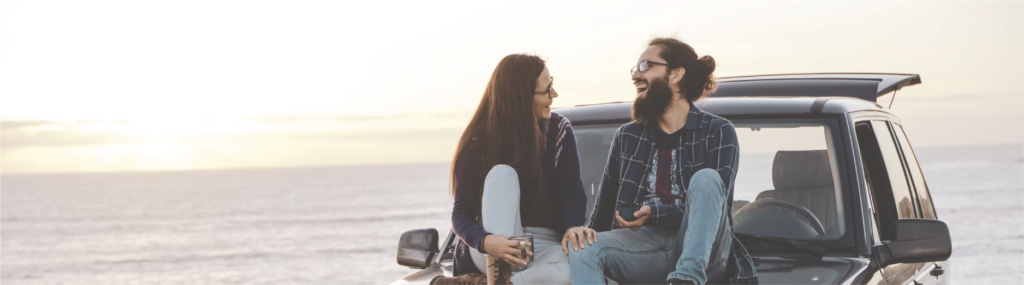 couple sitting on top of car hood laughing together