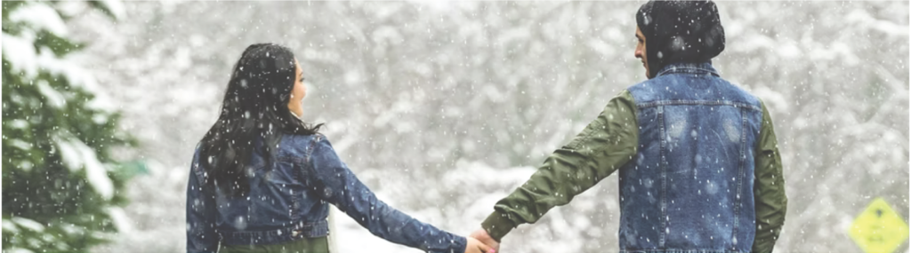 Couple holding hands, looking at each other walking down snowy street