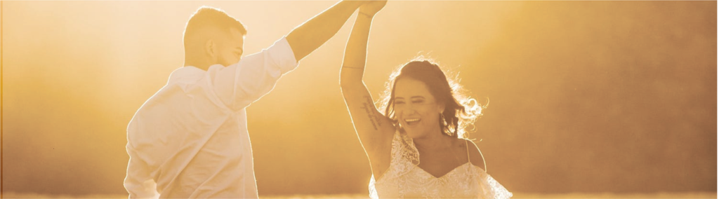 Cheerful newlywed couple dancing on sandy coast on sunny day